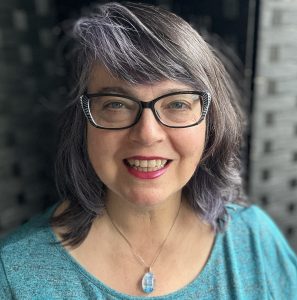 Izolda headshot. Woman wearing a teal top with a dark gray background
