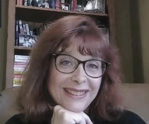 dawn barclay headshot - woman in front of bookselves with chin in hand